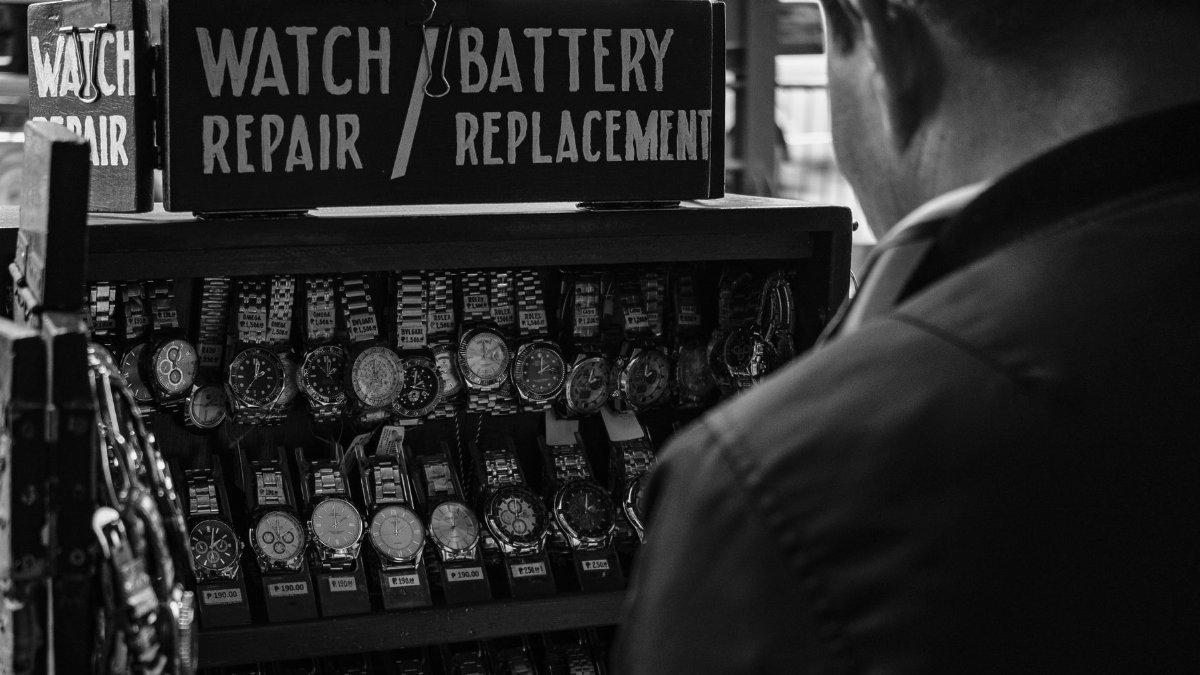 Monochrome image of a watch repair stand with various wristwatches and signage.