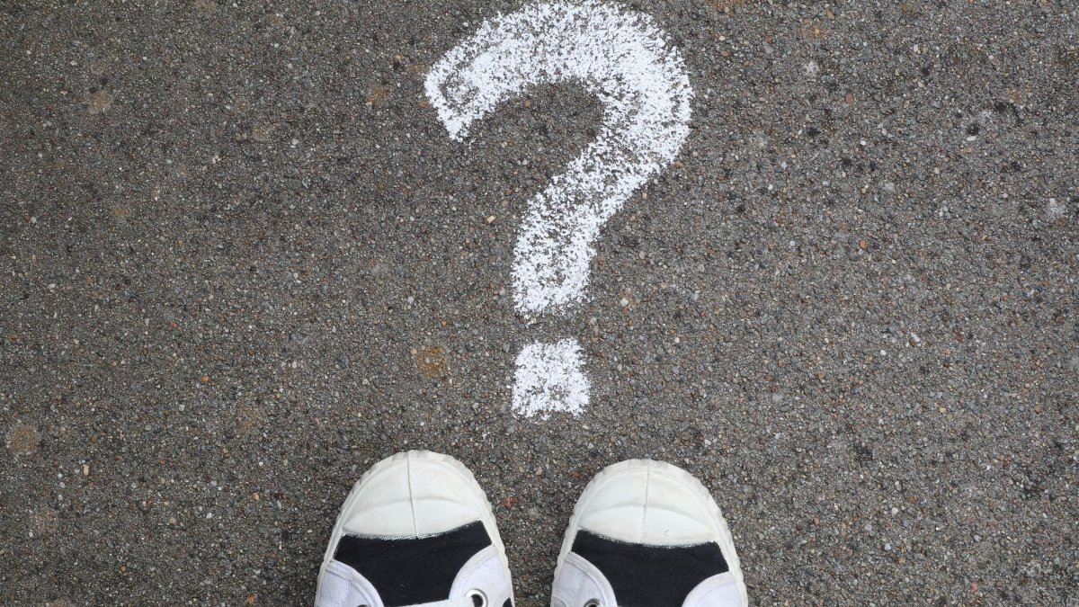 Sneakers on pavement with a chalk question mark, symbolizing curiosity or decisions.