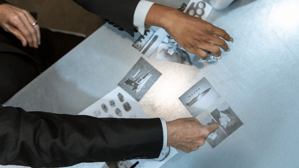 Detectives analyzing black and white photos and fingerprints. Investigation process depicted in detailed top view.