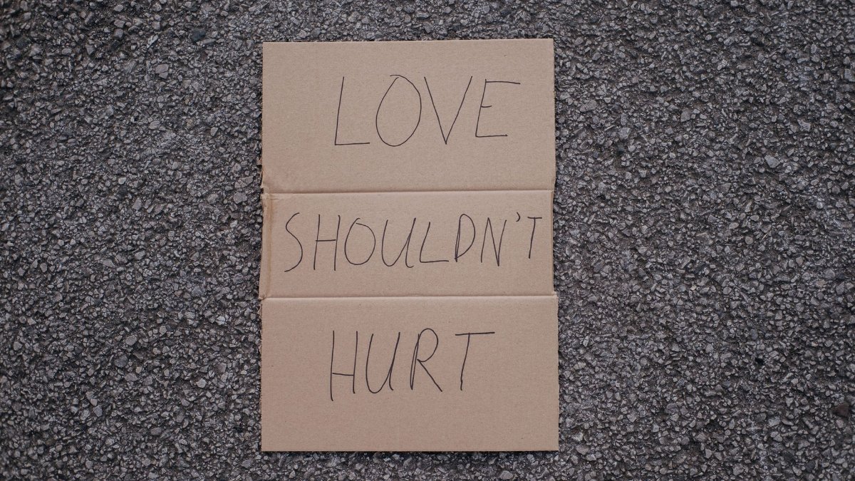 Top view of social slogan love should not hurt on cardboard placed on asphalt road on urban street