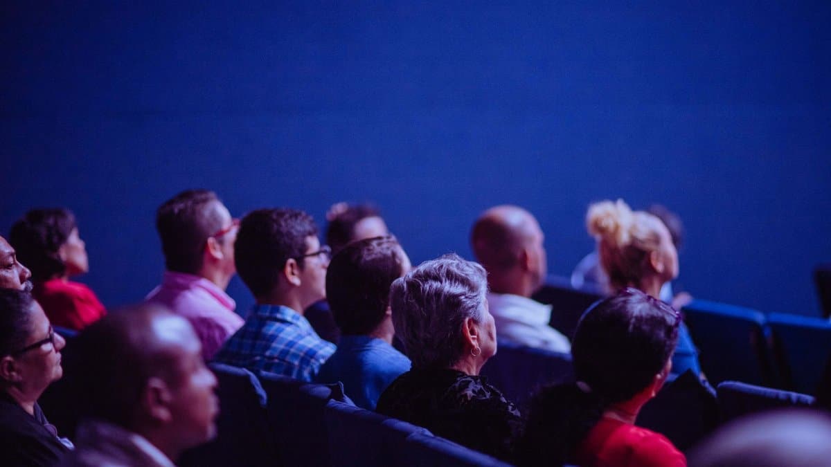 An attentive group of adults seated at an indoor conference, focusing on a presentation.