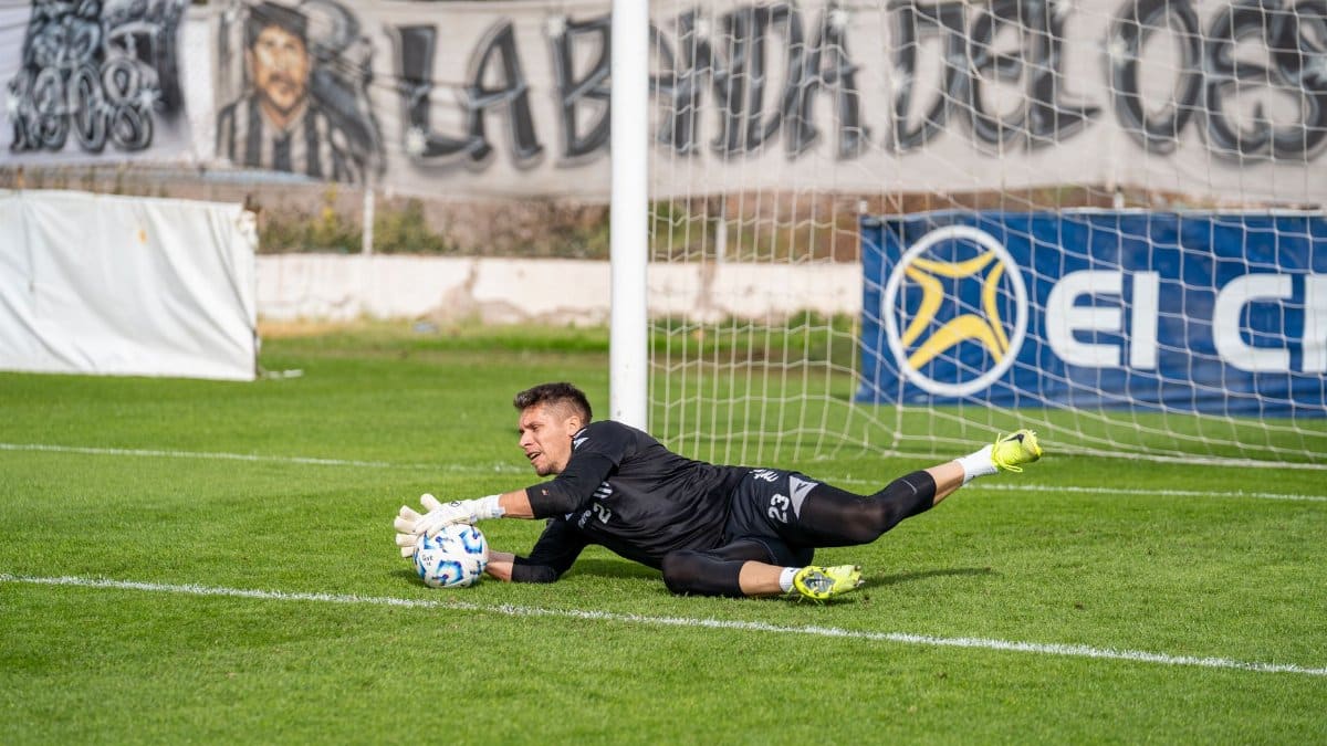 A goalkeeper in action making a dive save during a football match, showcasing skill and agility.