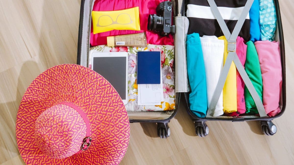 Top view of a suitcase packed with clothes, a camera, and a sun hat, ready for summer travel.