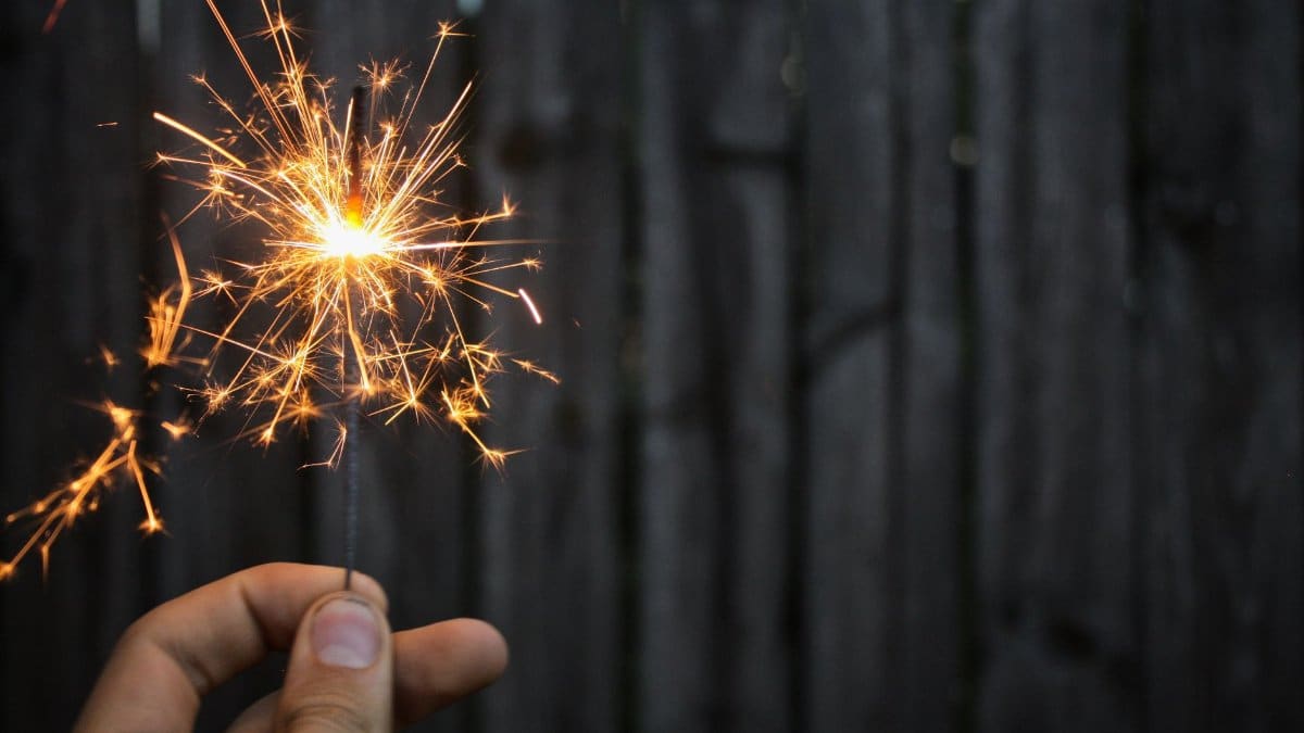 A person holds a sparkler with bright sparks against a dark background, creating a festive ambiance.
