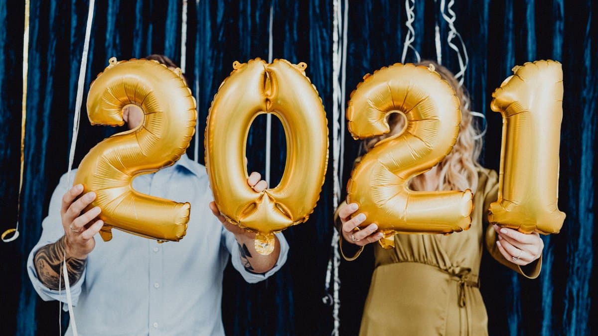 Two people holding golden 2021 balloons, celebrating a festive New Year event.