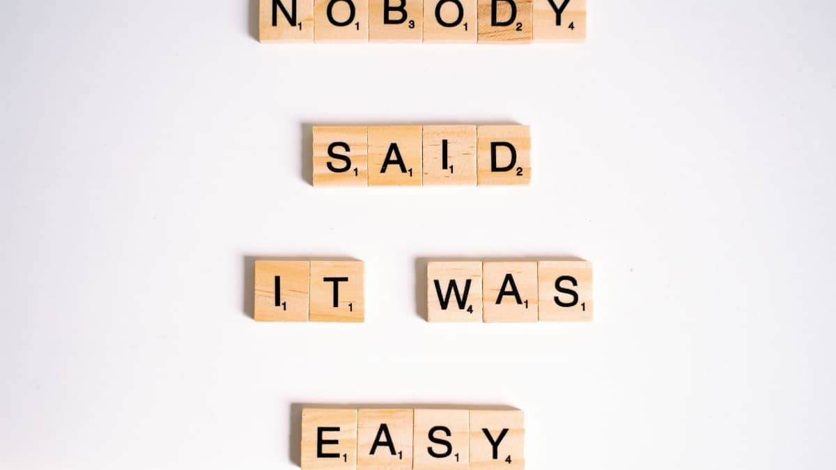 Close-up of wooden Scrabble tiles spelling 'nobody said it was easy' on a white background.