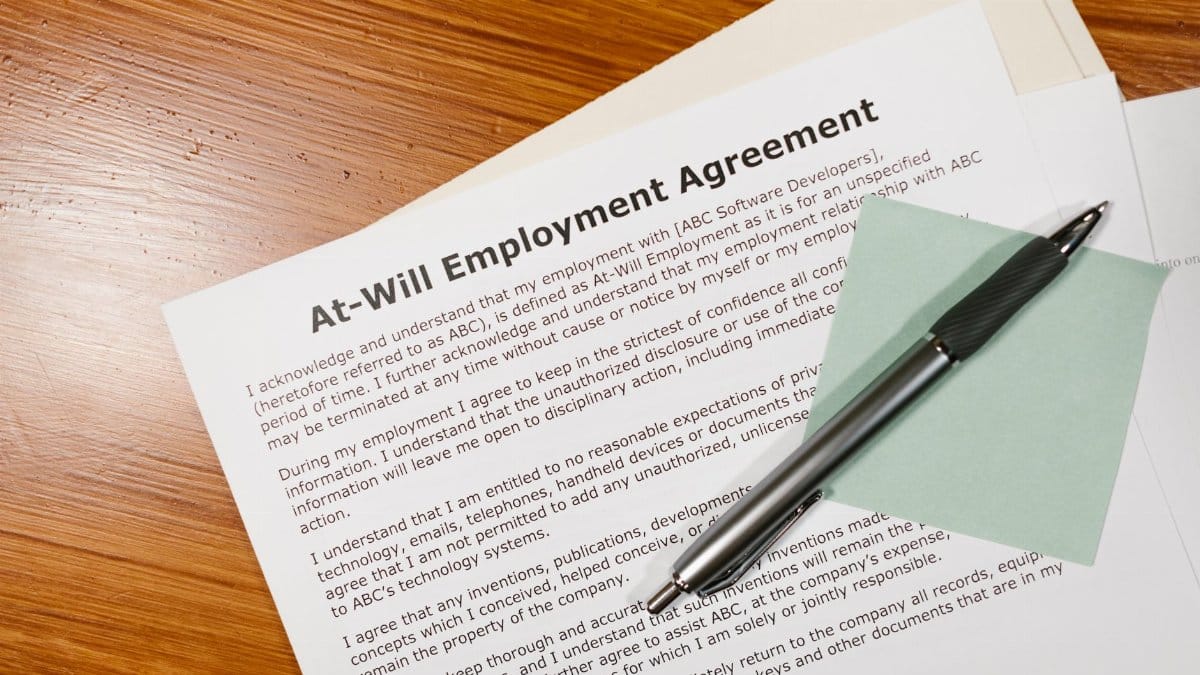 Close-up of an at-will employment agreement on a wooden desk with a pen, emphasizing legal and business concepts.