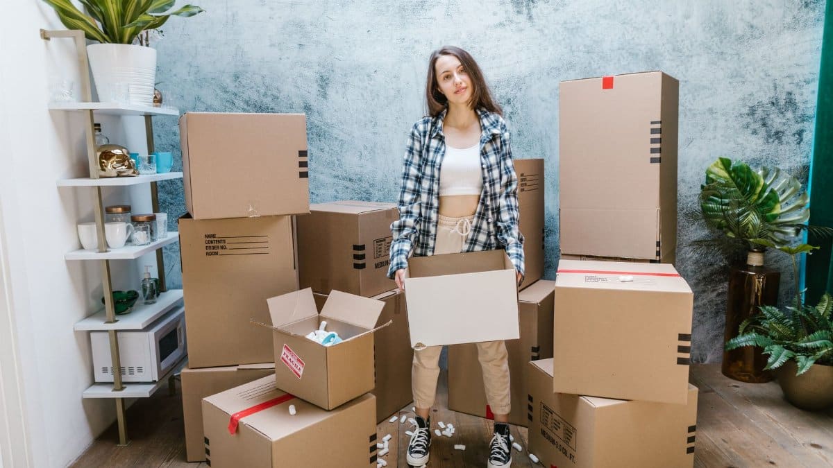 A woman organizing cardboard boxes filled with packing materials in a sunlit living room, preparing for a move.