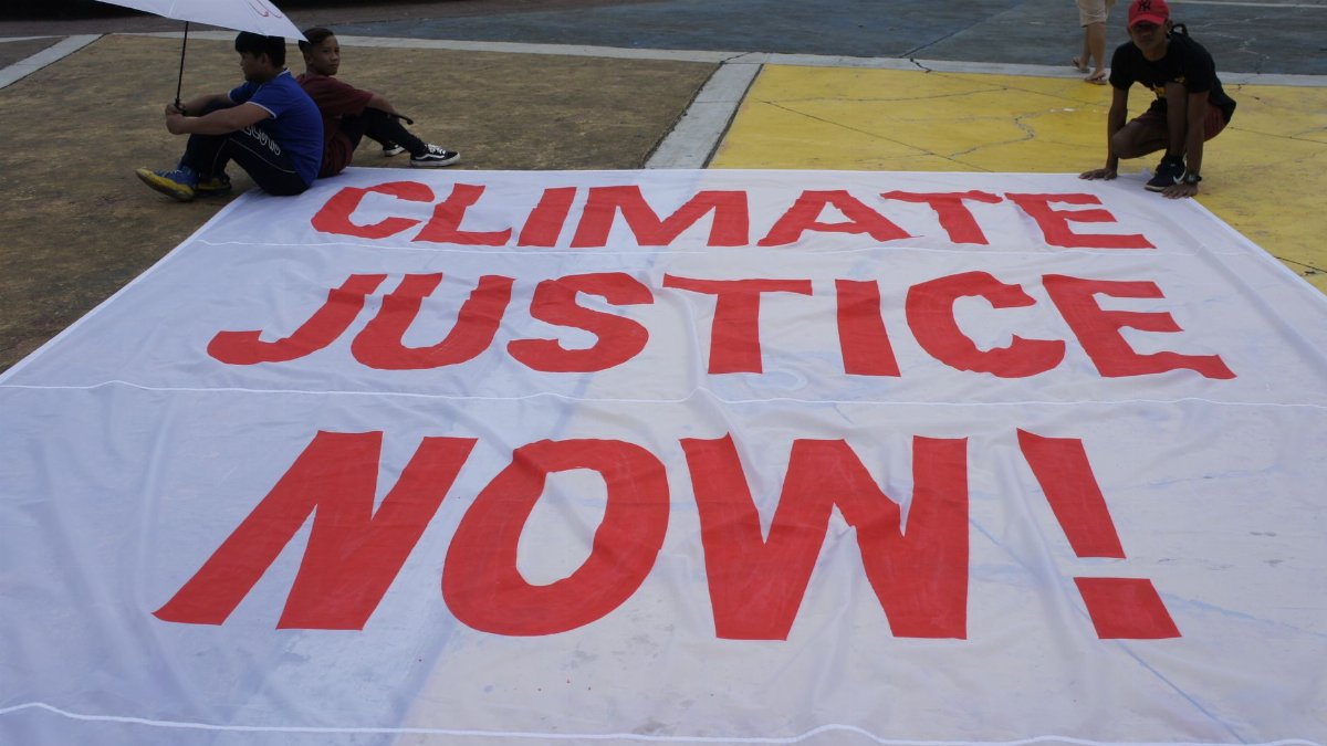 Large protest banner reading 'Climate Justice Now!' displayed outdoors during a demonstration.