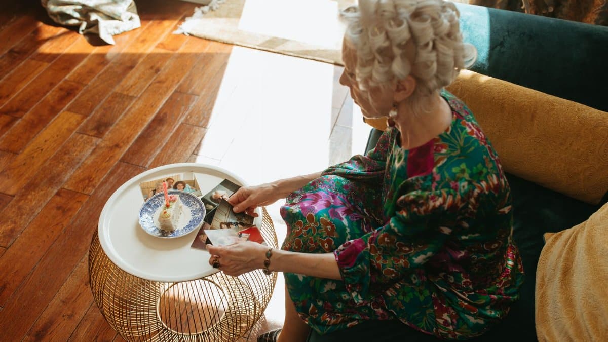 Senior woman with curlers reminiscing over old photographs in a cozy living room.