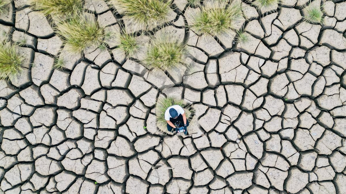 Drone captures a man sitting on dry, cracked earth amidst an arid landscape.