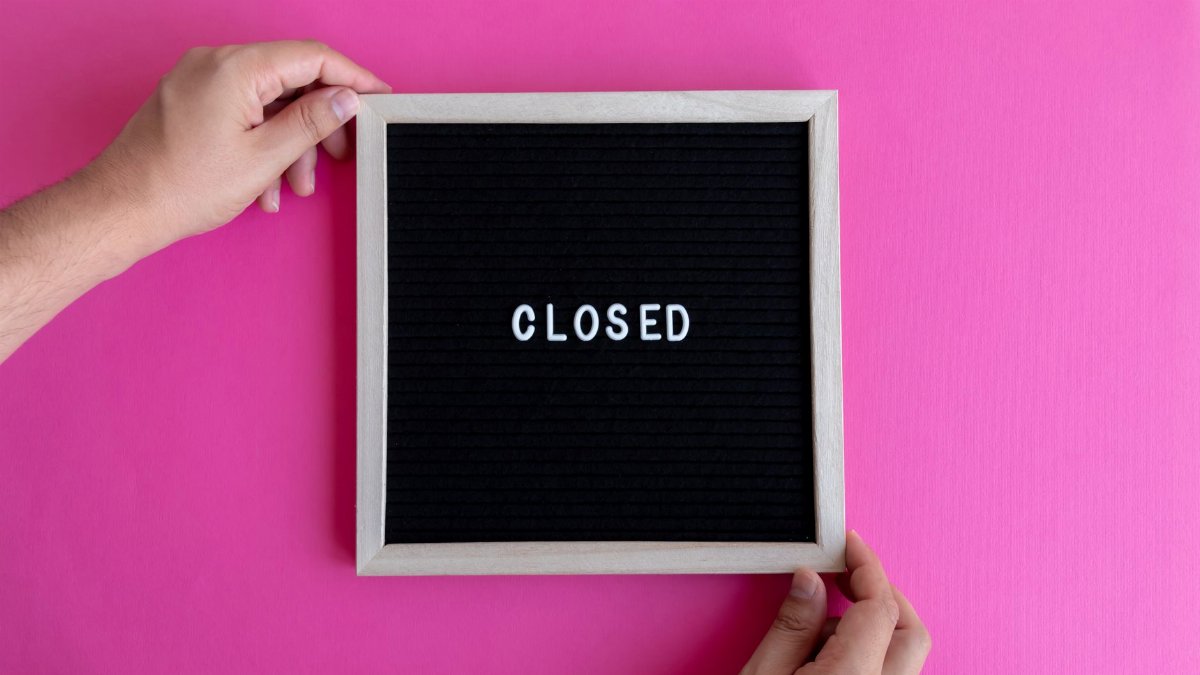 Hands holding a blackboard with 'Closed' text on a vibrant pink background, conveying closure or unavailability.