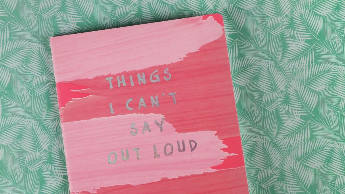 Pink notebook with the text 'Things I Can't Say Out Loud' on green leafy surface.