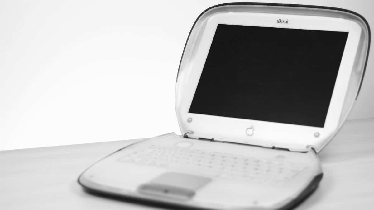 Classic iBook laptop with keyboard and screen displayed on a desk in monochrome.
