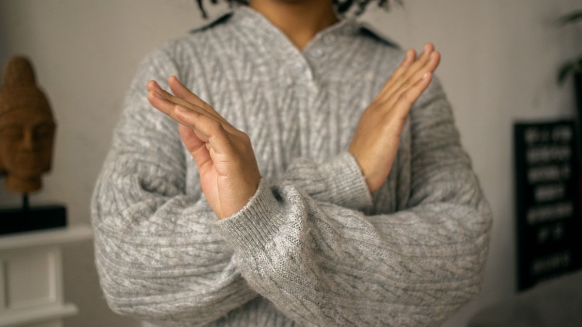 Crop faceless African American woman in warm gray sweater showing prohibit gesture in light room