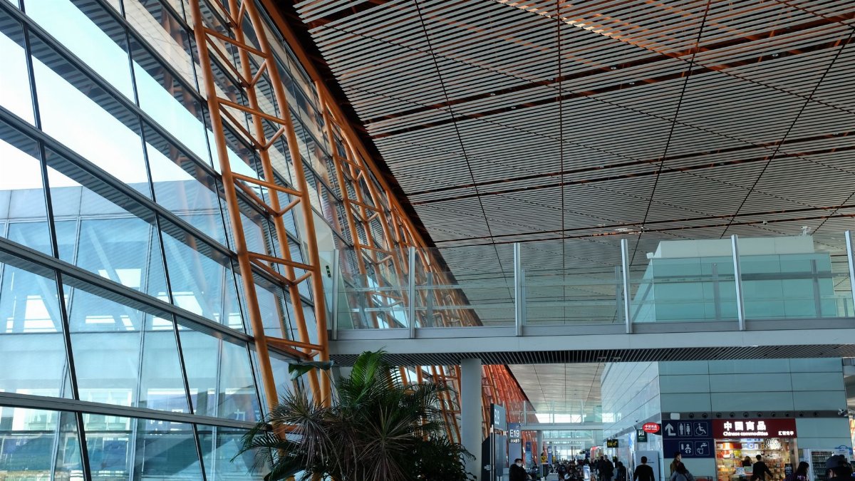 Wide-angle view of a bustling airport terminal featuring modern geometric architecture and natural lighting.