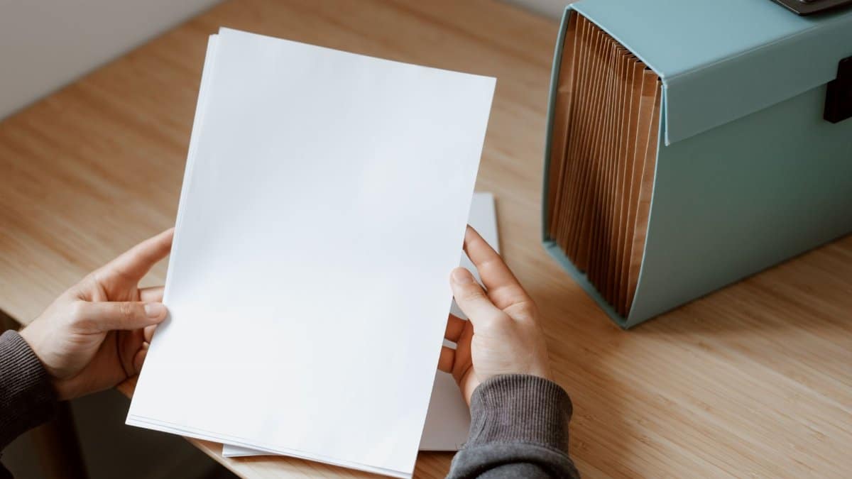 From above of crop unrecognizable person selecting sheet of paper against briefcase for documents