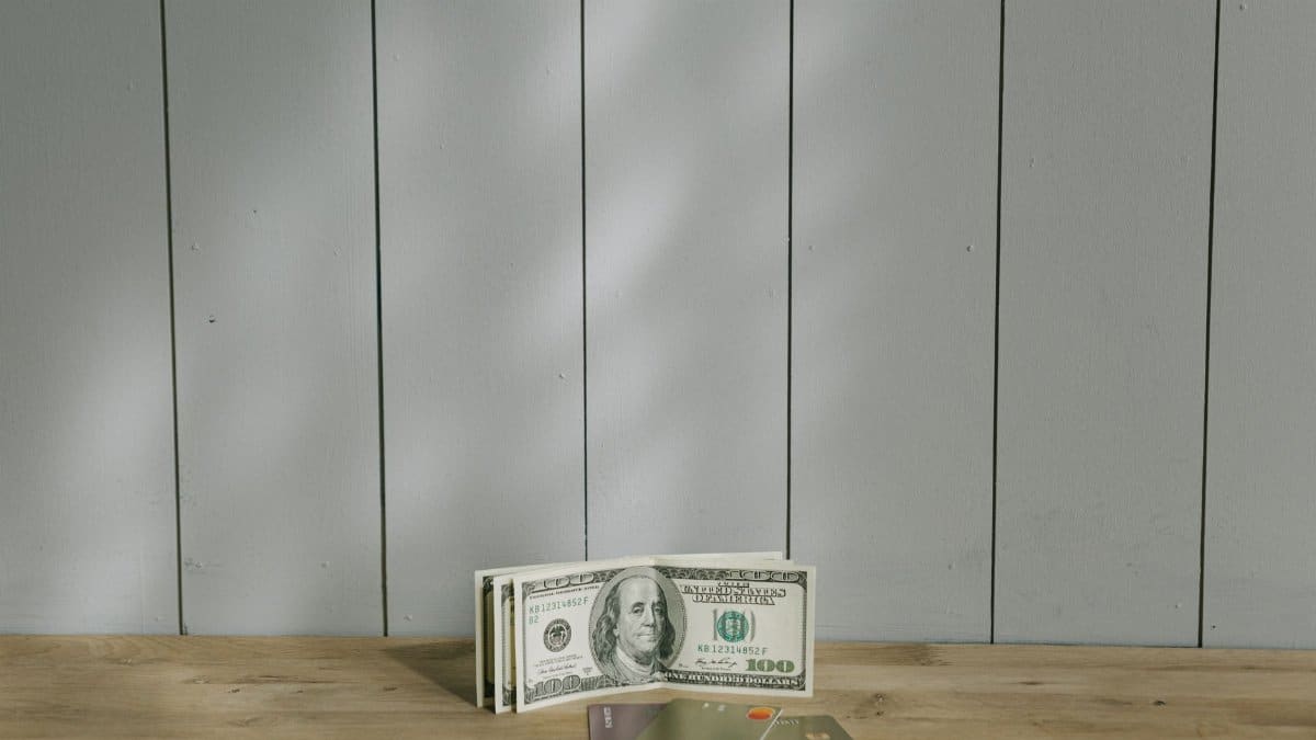 A stack of hundred-dollar bills and credit cards on a wooden surface with a neutral background.