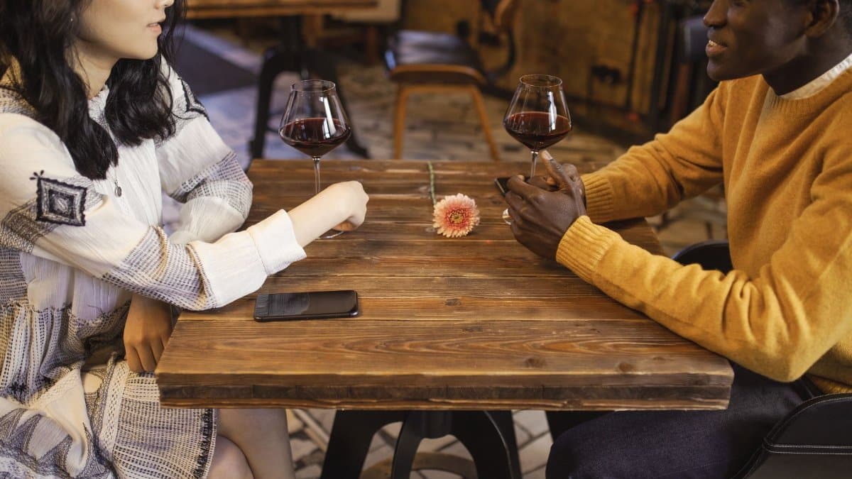 Interracial couple enjoying a romantic date with wine in a cozy café setting.