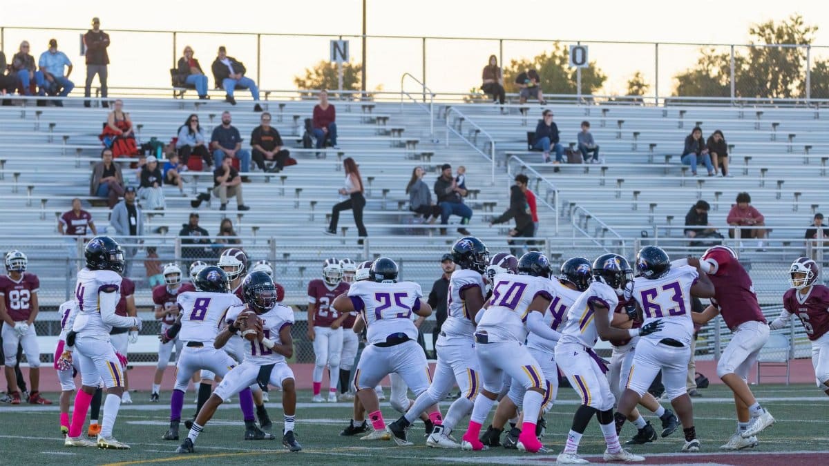 Players compete in a high school American football game with fans in the bleachers.
