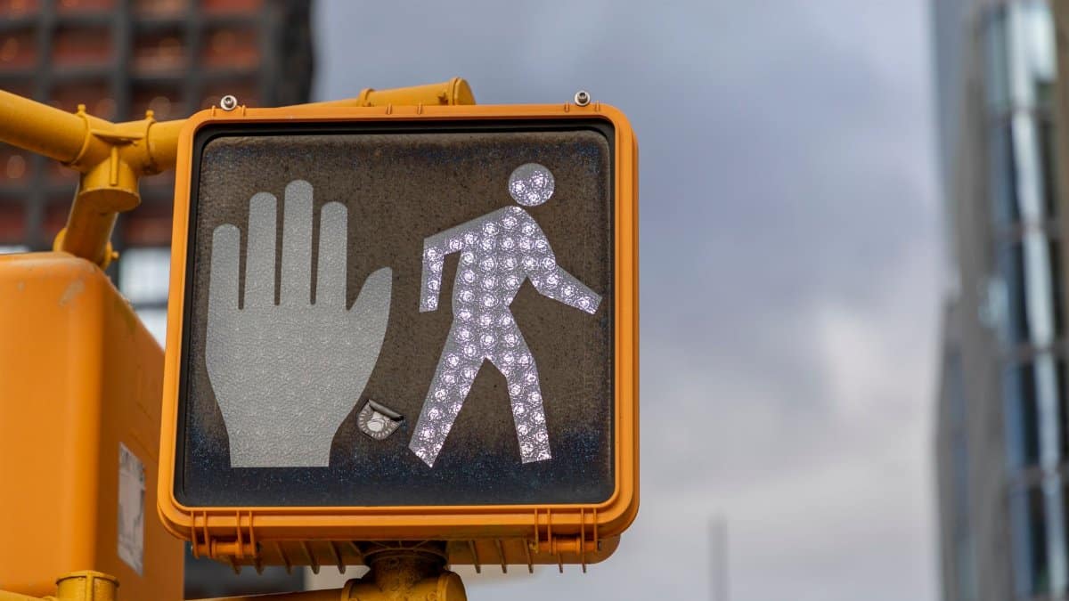 Street view of an illuminated pedestrian crosswalk signal with buildings in the background.