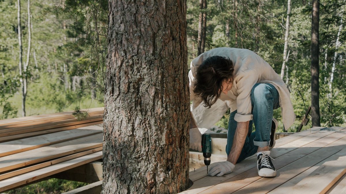 A man performs manual labor using a drill on a forest boardwalk construction project.