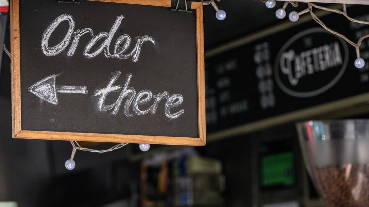 Chalkboard sign directing to order inside a cozy cafe with festive lights.