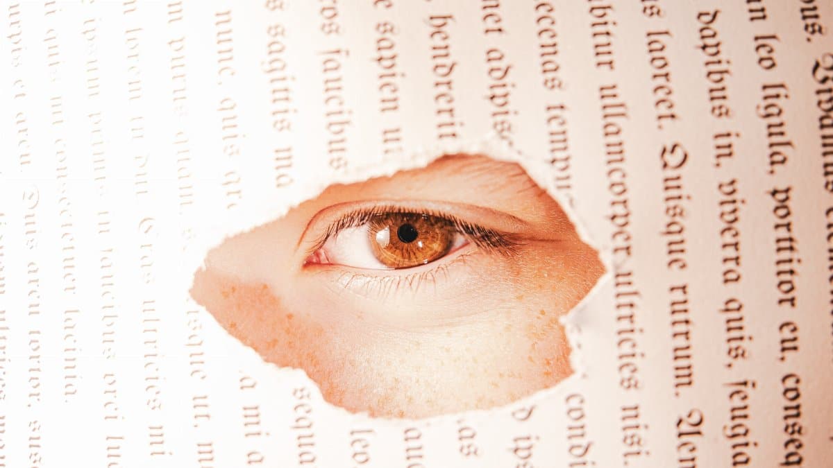 A close-up of an eye seen through a torn book page, creating a conceptual visual.