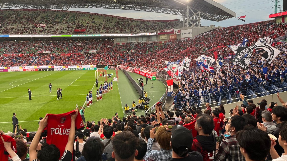 A thrilling soccer match at a packed stadium with energetic fans waving flags and cheering in Japan.