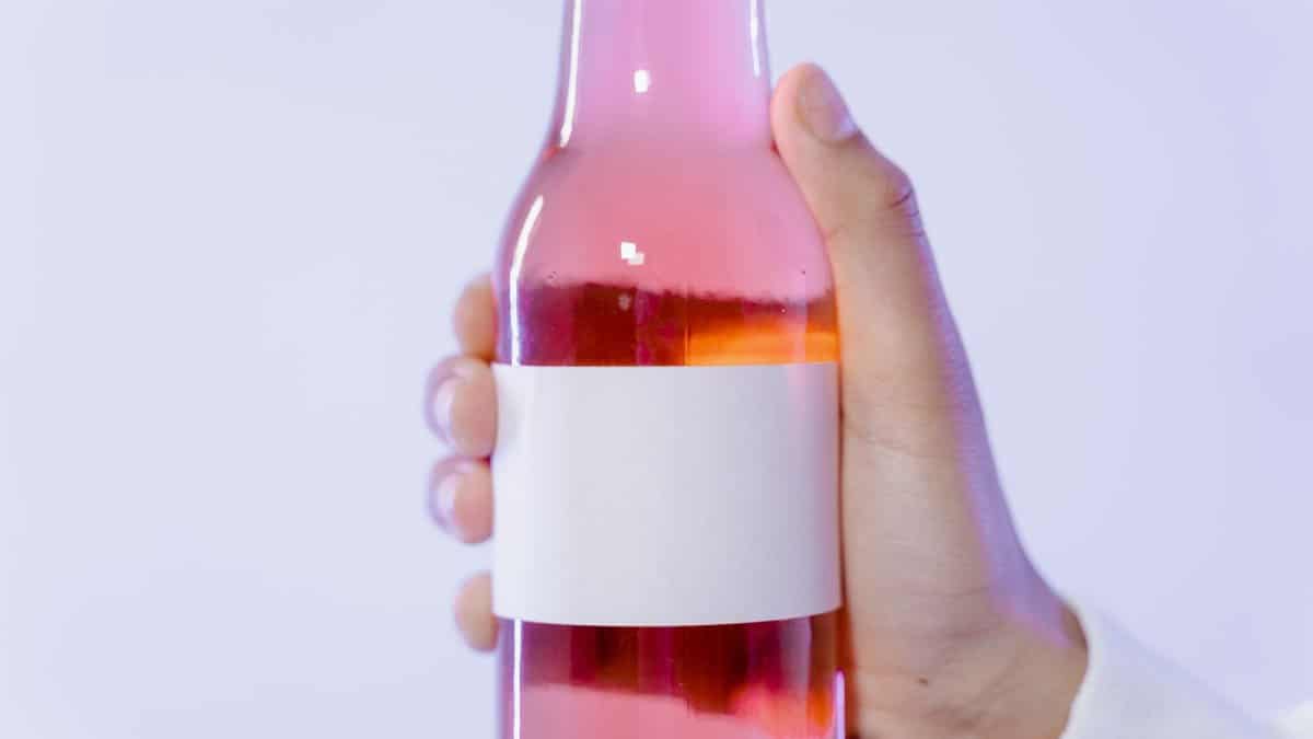 Close-up of a hand holding a pink glass bottle with a blank label for design.