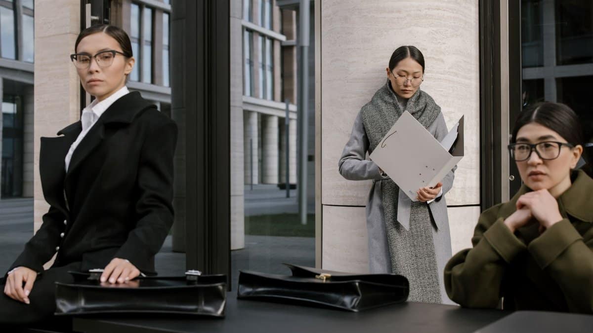Three professional women in formal outfits with briefcases, posing outside a modern office building.