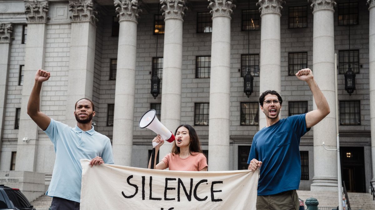 Group of activists raising fists and chanting with a protest banner outside a government building.