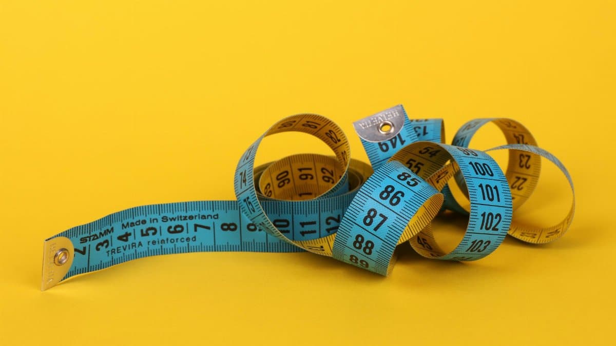 Colorful measuring tape curled up on a vibrant yellow background, ideal for design concepts.