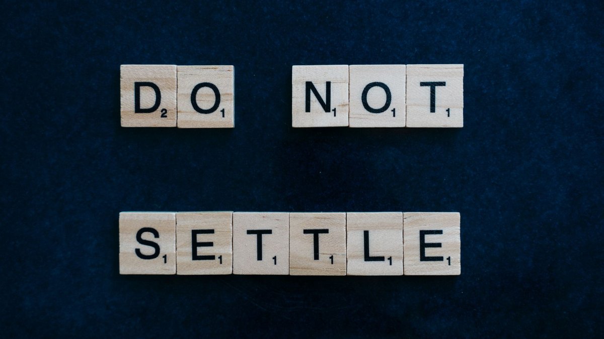 Wooden Scrabble tiles spelling 'Do Not Settle' on a dark surface, top view.