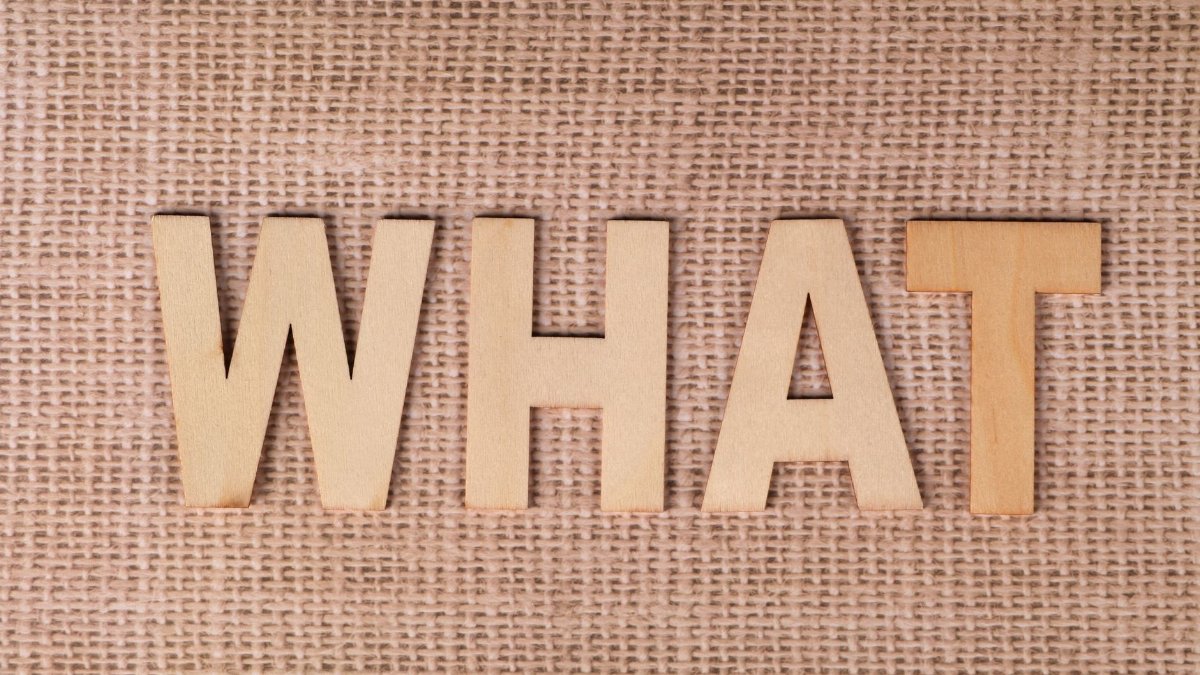Wooden letters forming the word WHAT set on a textured burlap surface.
