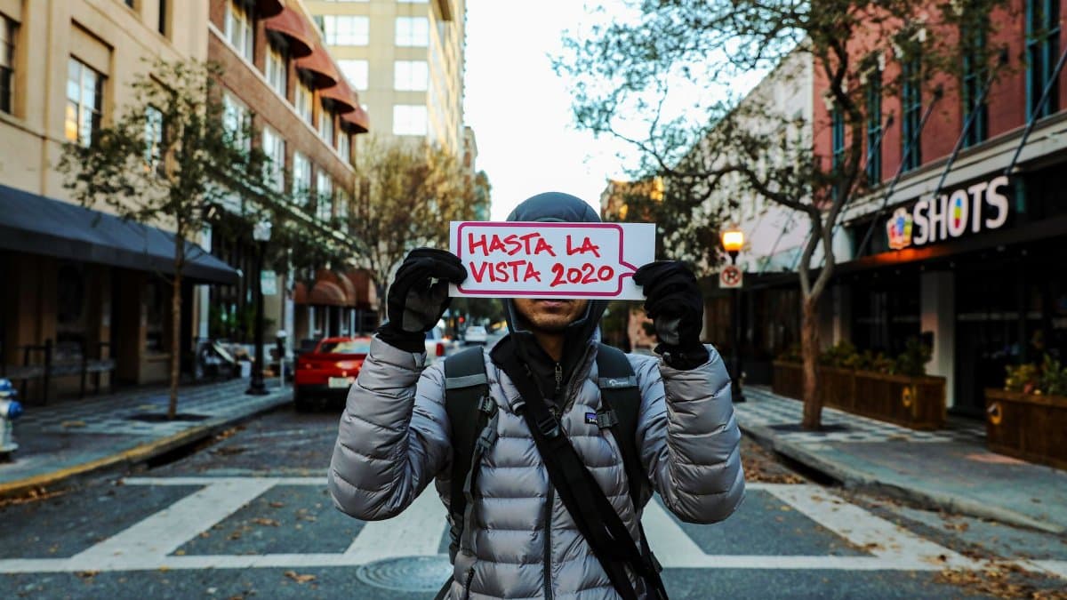 Person in warm clothing holds a 'Hasta La Vista 2020' sign on a street in Orlando, Florida.