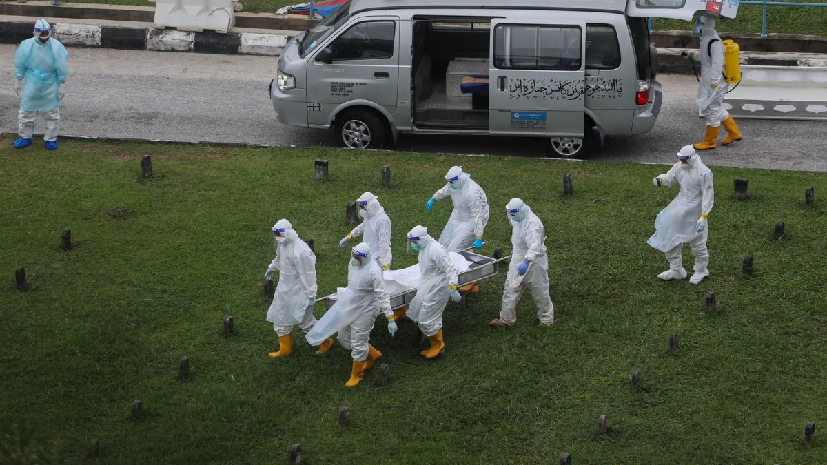 Healthcare workers wearing PPE carry a stretcher near a medical van in Kuala Lumpur.