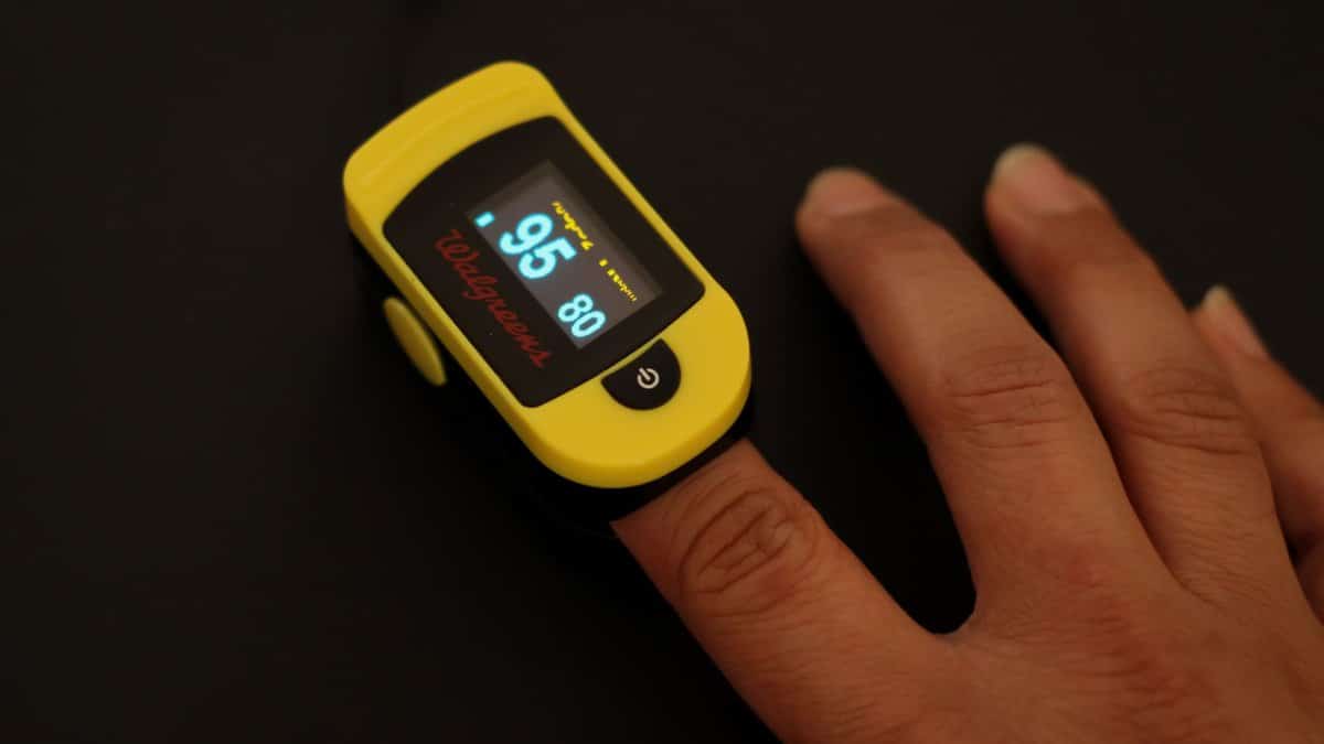 A close-up shot of a yellow pulse oximeter measuring oxygen levels on a finger.