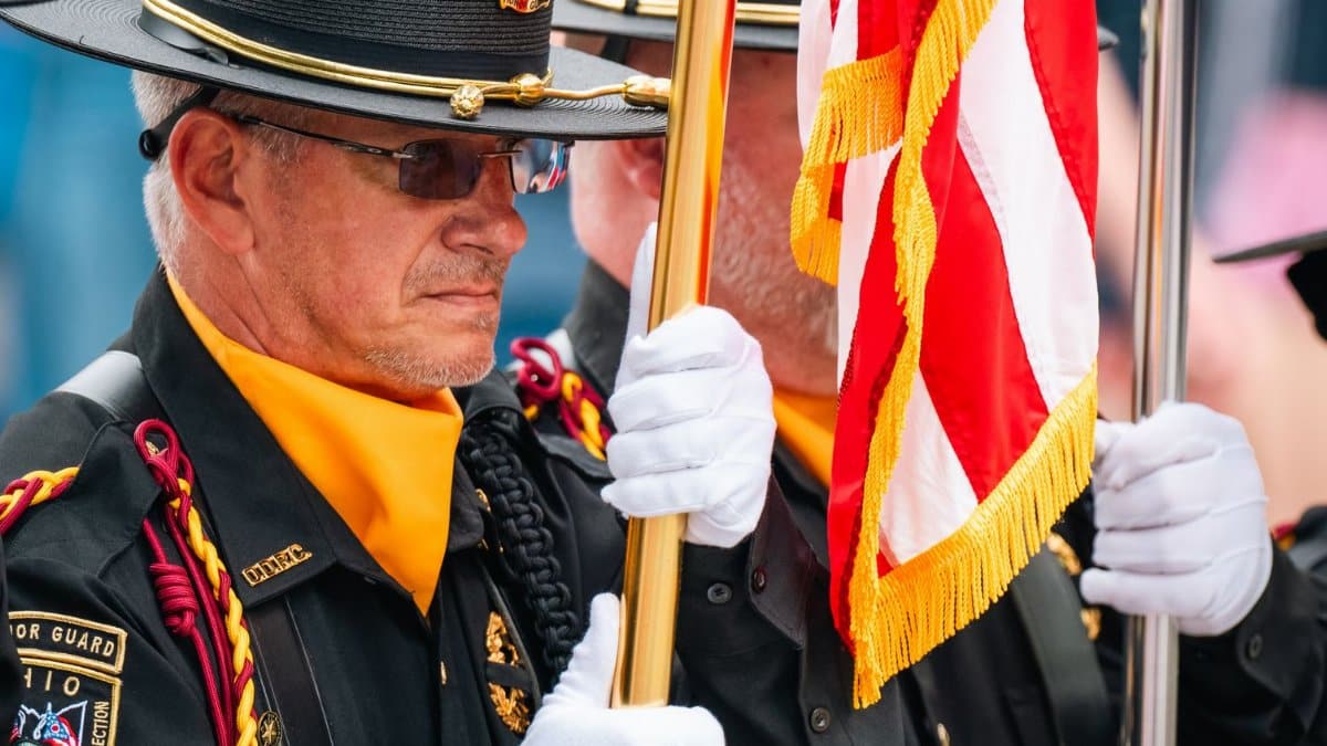 Honor Guard members in uniform holding an American flag during a formal ceremony.