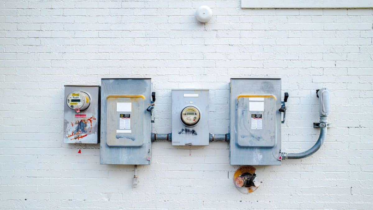 Electrical boxes and power meters mounted on a white brick wall.
