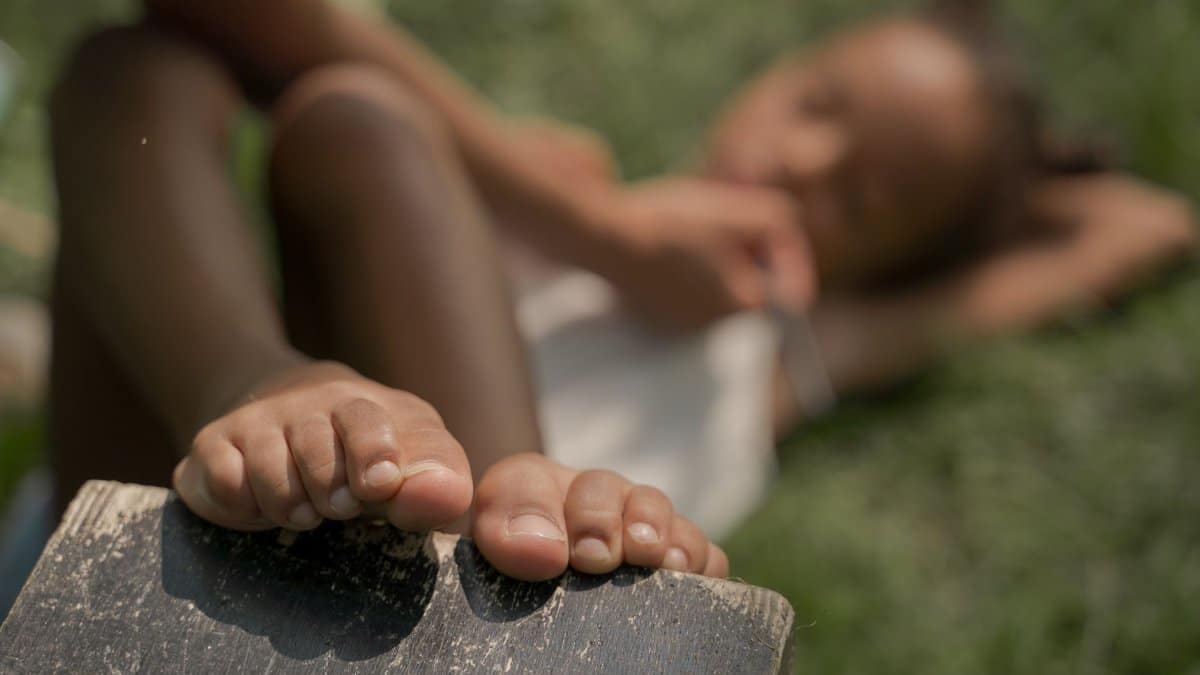 A child laying on the grass, enjoying a sunny summer day with a focus on bare feet.