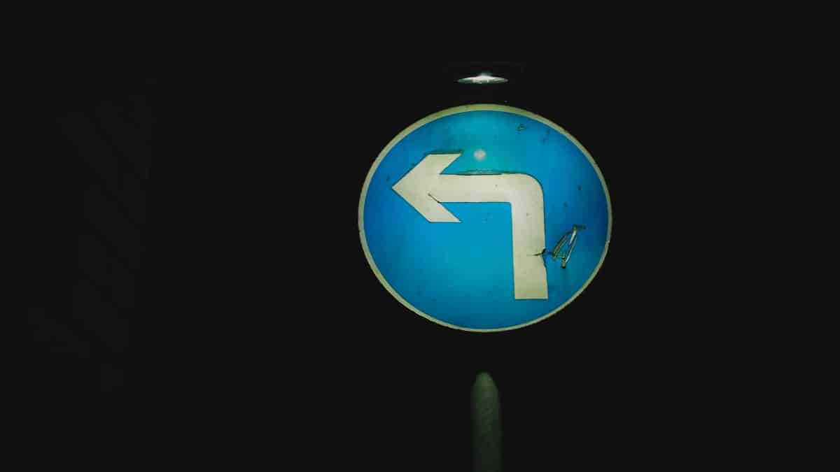 Round old left turn sign on blue background with light at dark night