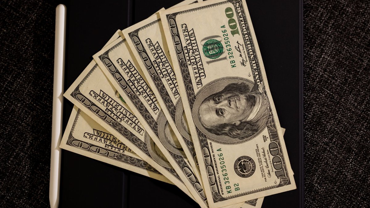 Spread of US dollar bills on black surface with stylus, symbolizing finance and technology.