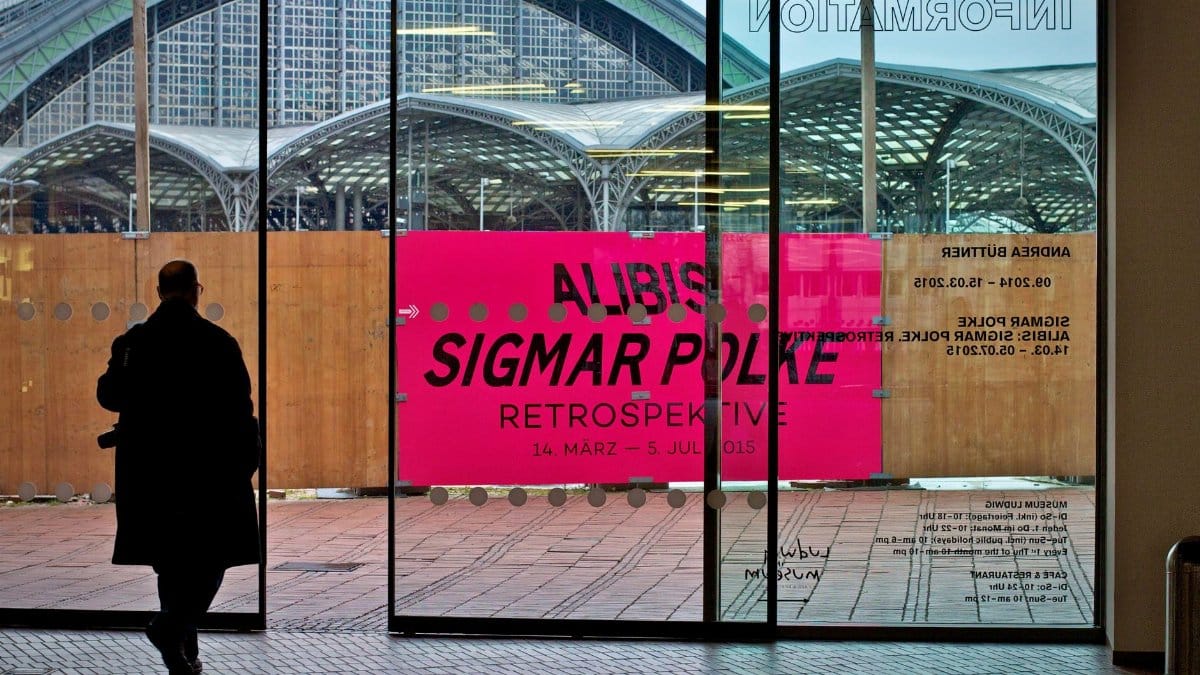 A silhouette of a man walking past an art exhibition poster at a gallery entrance.