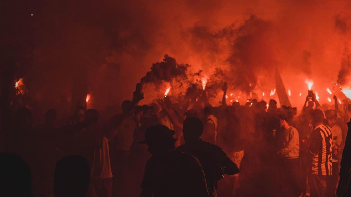 An energetic night celebration with people holding flares amidst smoke and vibrant flames.