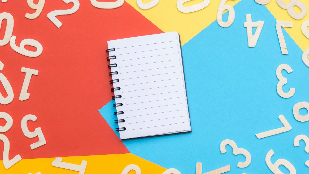 A spiral notebook surrounded by wooden numbers on a colorful geometric background, featuring red, yellow, and blue.