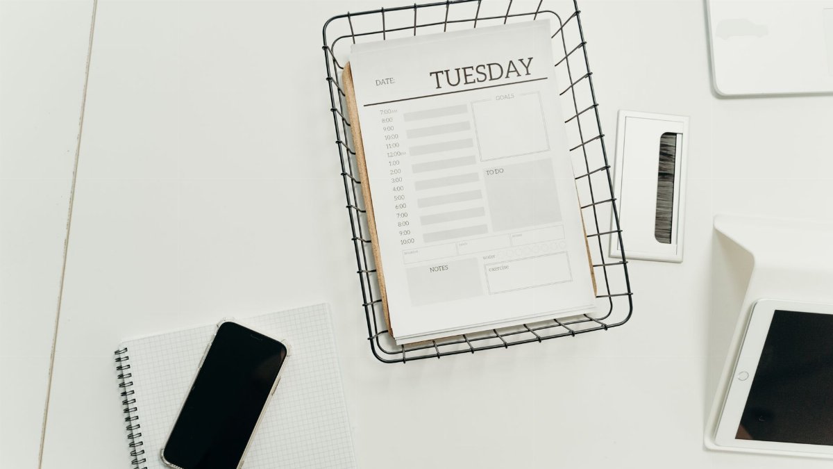 Top view of a neat office desk with a Tuesday planner, smartphone, and gadgets, perfect for scheduling and organization.
