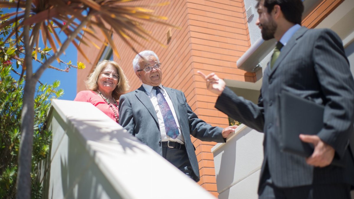 Elderly couple touring a modern home with a real estate agent in sunny Portugal.