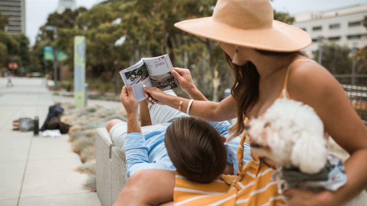 A couple enjoys a relaxing day outdoors, reading a book with their pet dog close by.