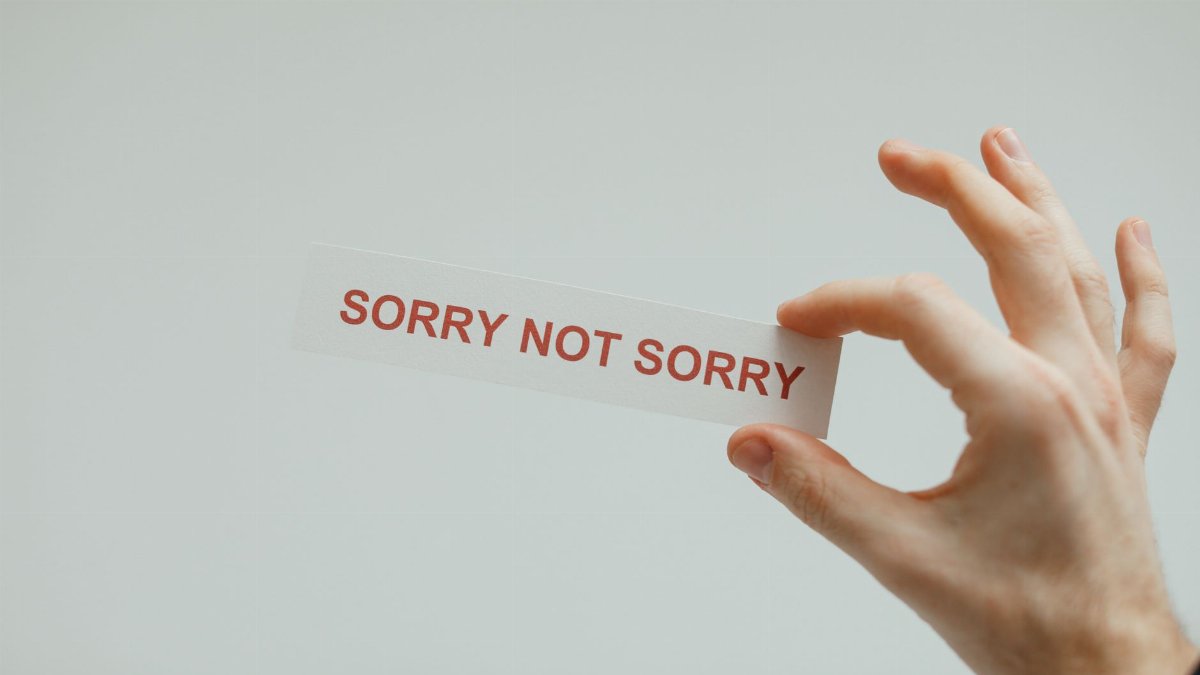 Hand holding a card with the phrase 'Sorry Not Sorry' on a neutral background.